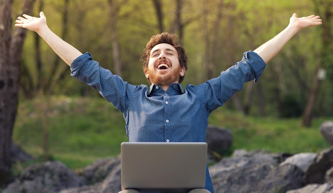 Ein Mann mit Laptop auf - Beruflicher Wechsel dem Schoß im Wald wirft glücklich die Arme hoch und freut sich über neuen Job